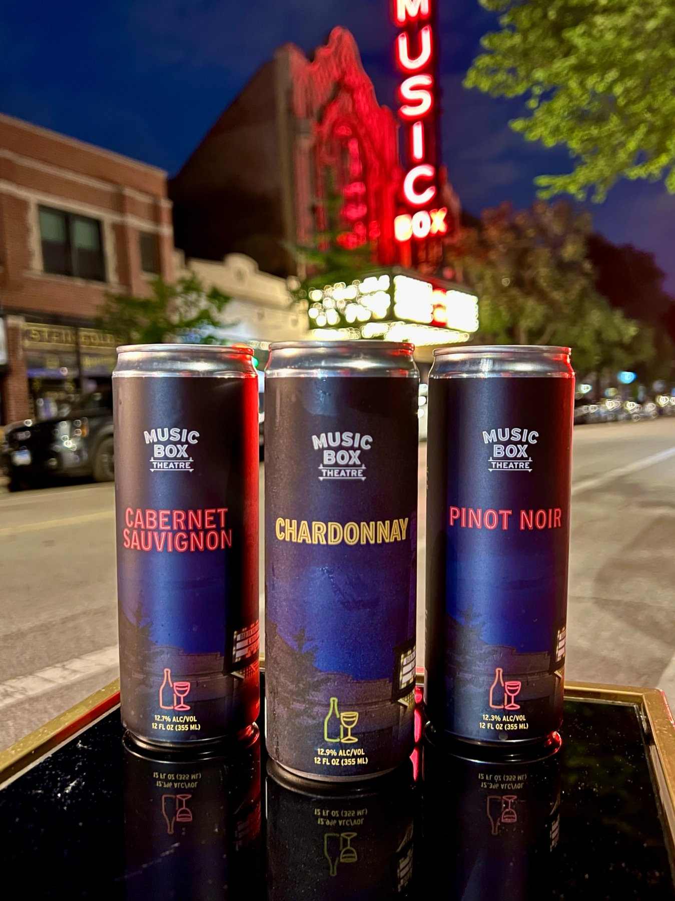 Music Box theatre branded wine cans (Cabernet Sauvignon, Chardonnay & Pinot Noir) with Music Box Theatre blurred in the background