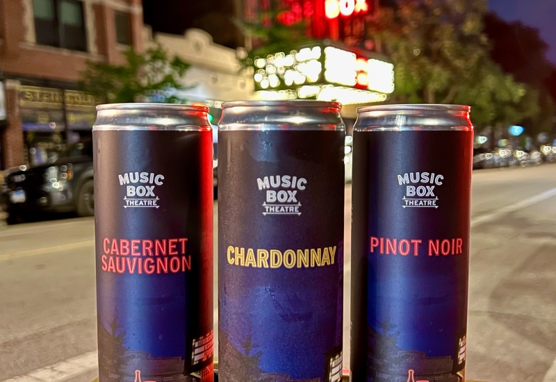 Music Box theatre branded wine cans (Cabernet Sauvignon, Chardonnay & Pinot Noir) with Music Box Theatre blurred in the background